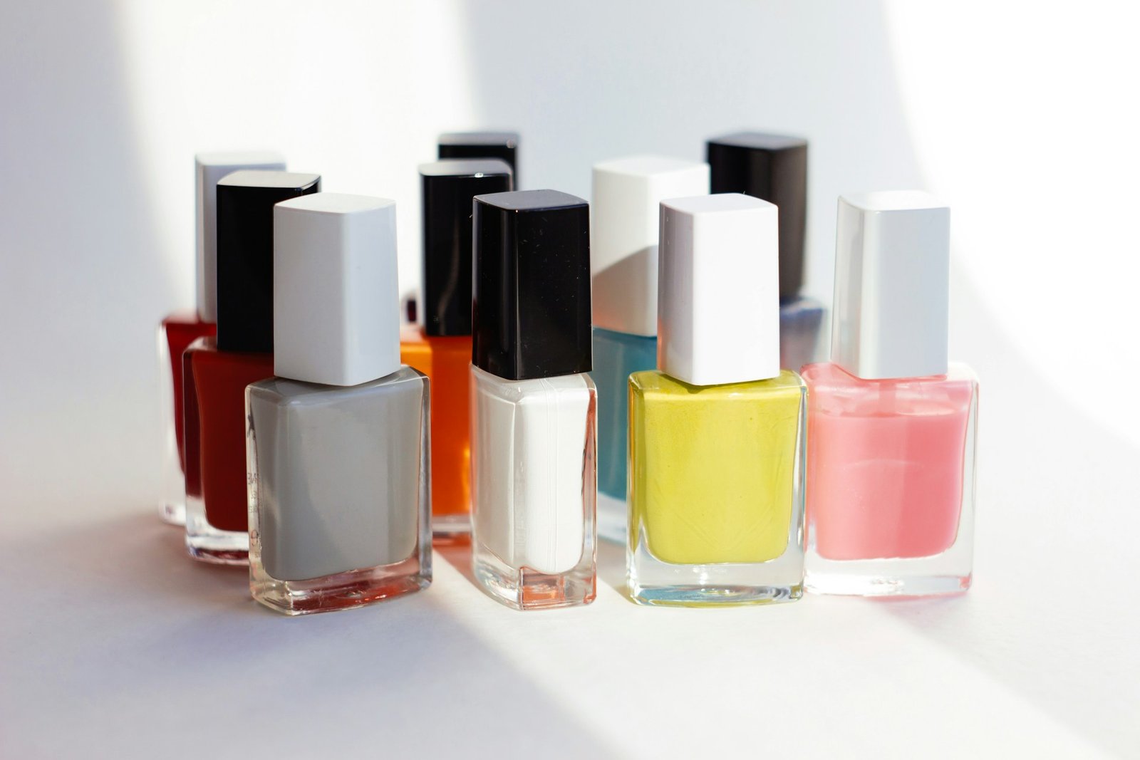 Varios frascos de esmalte de uñas de colores alineados sobre una superficie blanca