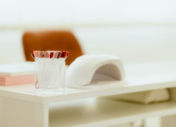 Lámpara de uñas LED blanca sobre una mesa de manicura clara, junto a un vaso con pinceles