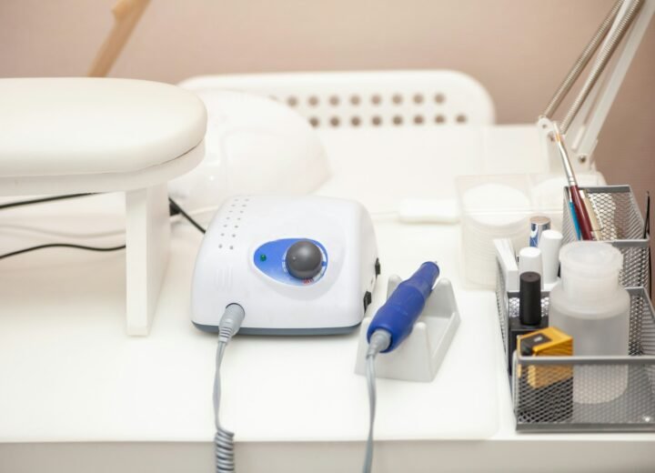 Torno de uñas eléctrico con su pieza de mano azul sobre una mesa blanca de manicura, junto a una lámpara y utensilios